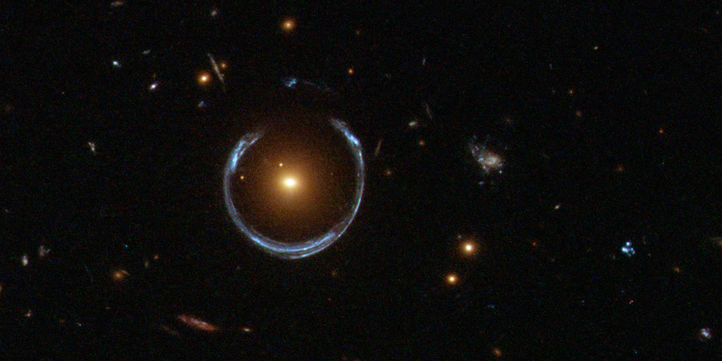 Obraz odległej, niebieskiej galaktyki zniekształcony przez efekt soczewkowania grawitacyjnego.