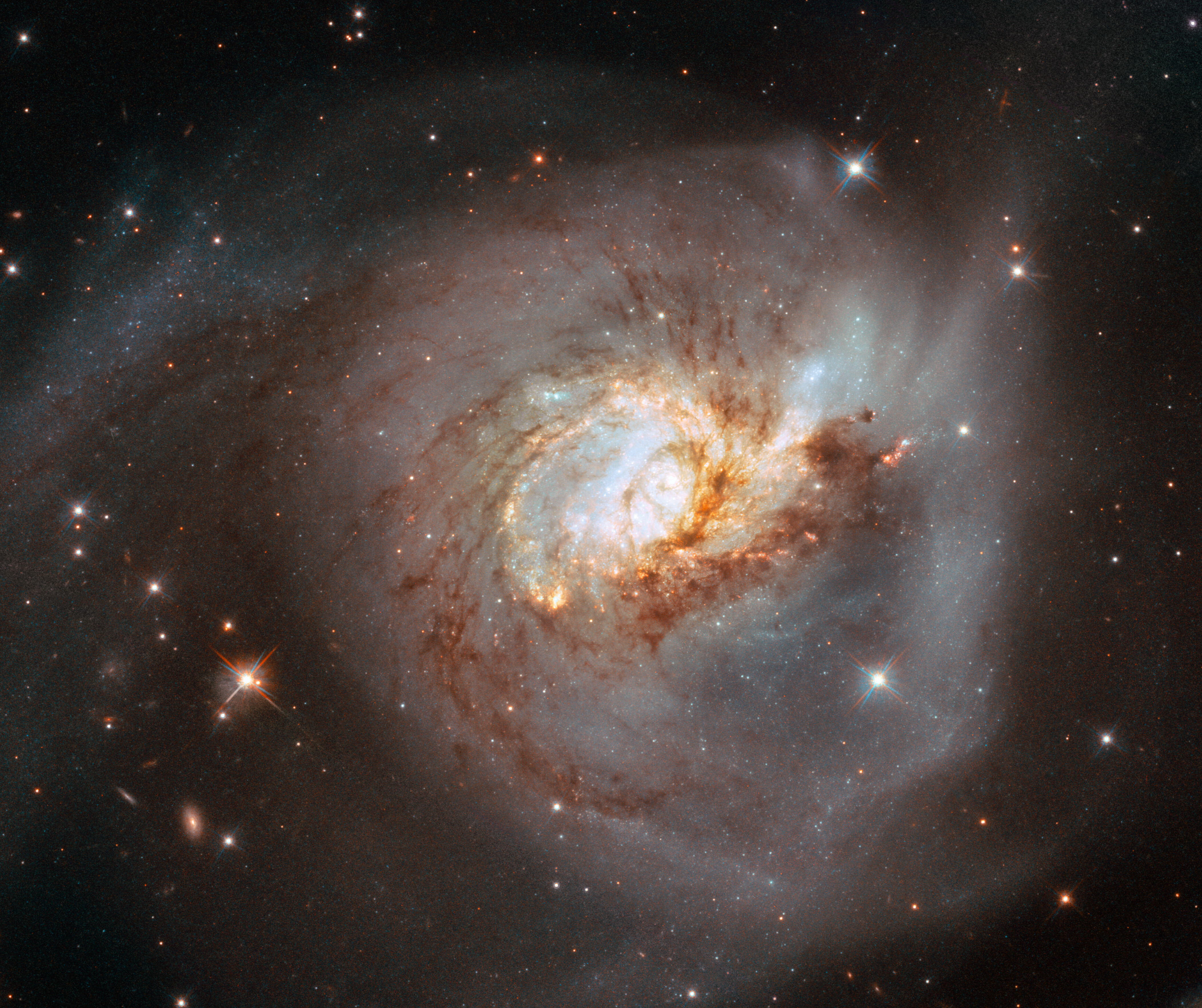 Na ilustracji: Obraz w zakresie optycznym spiralnej galaktyki NGC 3256 widzianej z boku. Został on uzyskany za pomocą Teleskopu Hubble’a. Widać szczegółowo ciemne włókna składające się z pyłu i gazu molekularnego, które wirują wokół centrów obu połączonych galaktyk. Gorące, masywne gwiazdy w obu jądrach galaktyk świecą jasno z odcieniem niebieskawym – mimo że ogólnie ta galaktyka jest jaśniejsza w podczerwieni. Źródło: ESA/Hubble, NASA