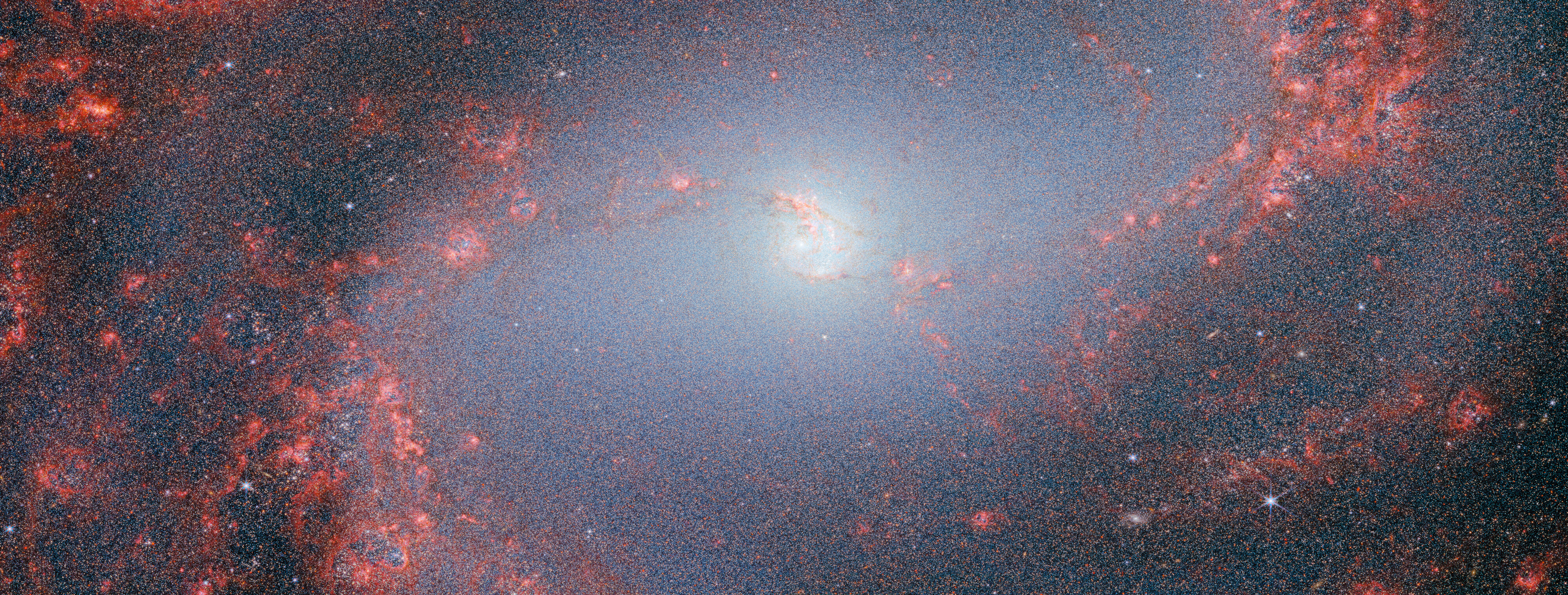 Na ilustracji: Zdjęcie galaktyki M83 (Galaktyka Południowy Wiatraczek) w bliskiej podczerwieni (~0,6μm-5μm) wykonane przez kamerę NIRCam z Teleskopem Webba. Widać jasne jądro galaktyki świecące promieniowaniem mnóstwa gwiazd. Największe zagęszczenie gwiazd jest w ramionach spiralnych. Oba ramiona są rozjaśnione przez obłoki gazowe w kolorze czerwonym i łączą się z centrum galaktyki. Materia gazowa tworzy nitkowate struktury w okolicach centralnych galaktyki i dalej staje się grubsza wzdłuż ramion spiralnych. Źródło: ESA/Webb, NASA & CSA, A. Adamo (Stockholm University) and the FEAST JWST team