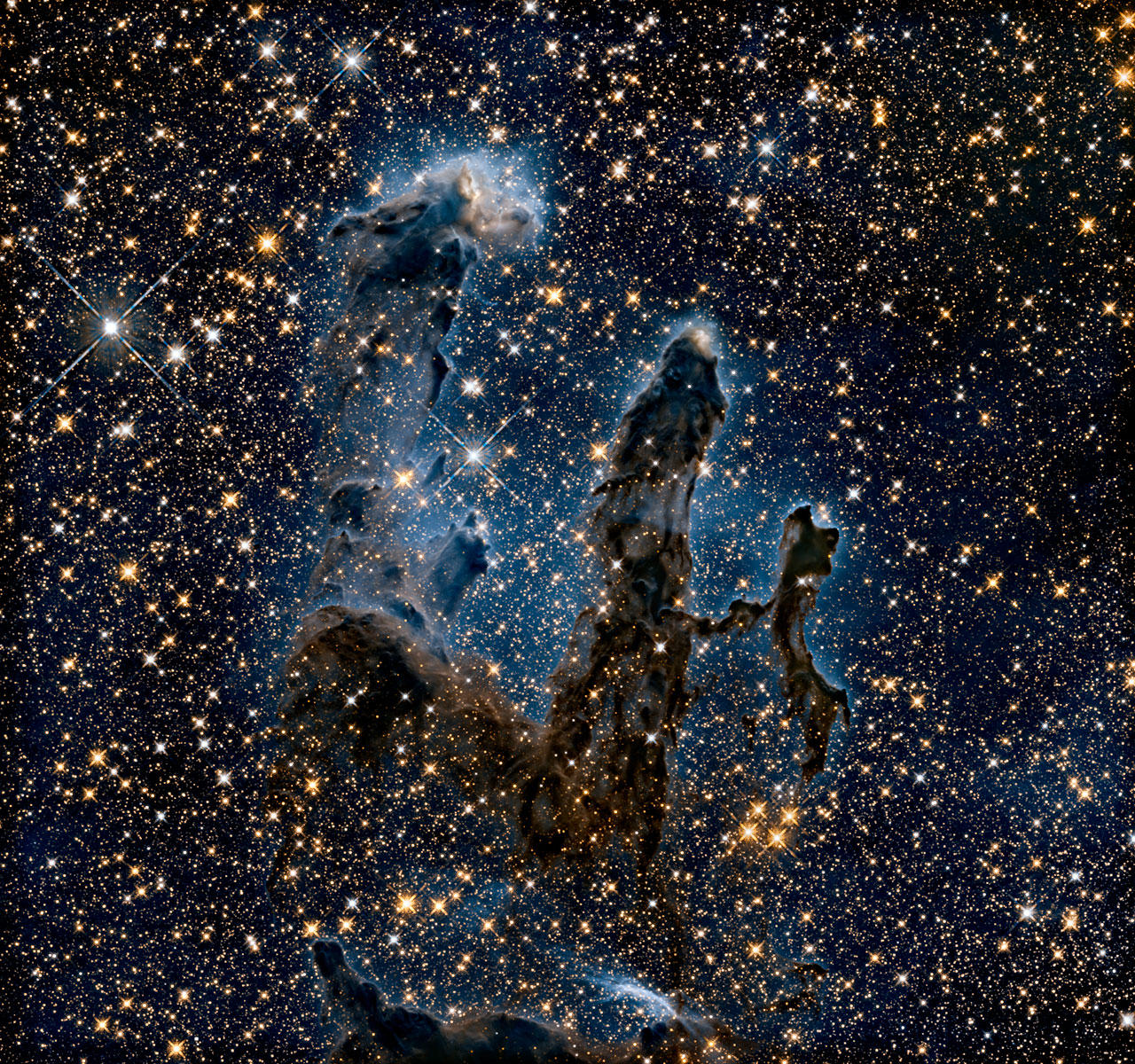 Promieniowanie podczerwone przenika przez gaz i pył, odsłaniając upiorne zarysy słupów, przez które przebija się światło niedawno narodzonych gwiazd. Źródło: NASA, ESA/Hubble and the Hubble Heritage Team