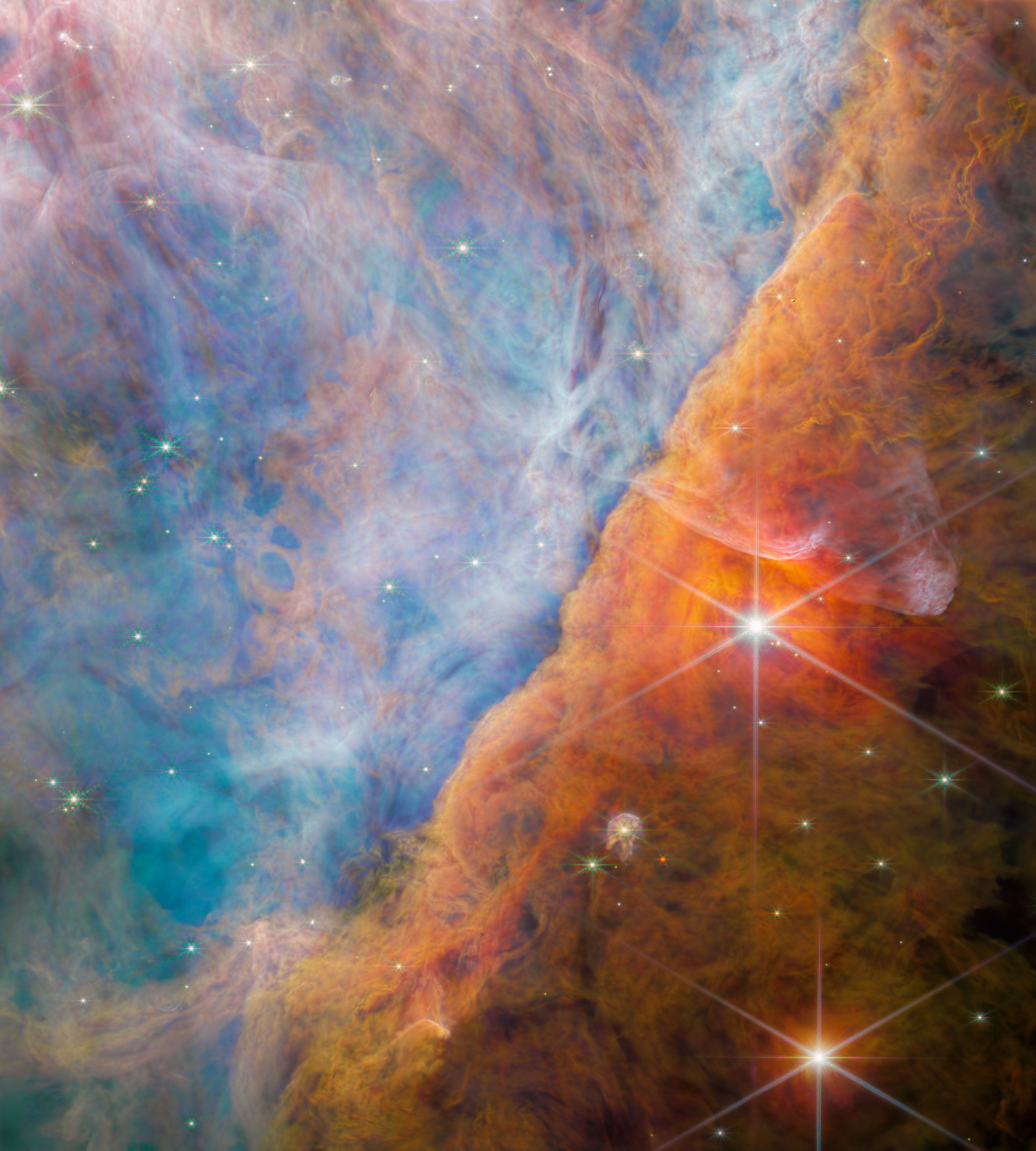Zdjęcie fragmentu Mgławicy Oriona zwanego Poprzeczką Oriona (ang. Orion Bar – nie mylić z asteryzmem zwanym Pasem Oriona / ang. Orion’s Belt) sfotografowane przez Teleskop Webba z kamerą NIRCam (bliska podczerwień: od 1,4μm/fiolet do 4,8μm/czerwień). W obszarze tej „poprzeczki” następuje oddziaływanie gęstych obłoków molekularnych z eultrafioletowym promieniowaniem pochodzącym od młodych i gorących gwiazd masywnych z pobliskiej Gromady Trapez znajdującej się tuż za górnym lewym narożnikiem zdjęcia. Silne promieniowanie UV pochodzące od tych masywnych gwiazd powoli niszczy Poprzeczkę Oriona oraz ma istotny wpływ na molekuły i chemię dysków protoplanetarnych, które powstały wokół rodzących się gwiazd. Źródło: ESA/Webb, NASA, CSA, M. Zamani (ESA/Webb), and the PDRs4All ERS Team