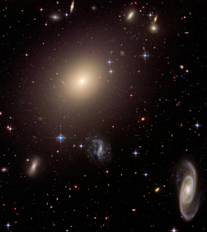 Fot. Zdjęcie gromady galaktyk Abel wykonane Kosmicznym Teleskopem Hubble'a. Na zdjęciu widoczne są galaktyki o różnorodnych kształtach. W centrum gromady widoczna jest gigantyczna galaktyka eliptyczna, w prawym dolnym narożniku piękna galaktyka spiralna, a wokoło wiele mniejszych obiektów o przeróżnych kształtach, rozmiarach i kolorach. Źródło: NASA/ESA/Hubble Heritage Team (STScI/AURA) - Roen Kelly 