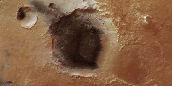 Na ilustracji: Meridiani Planum, na północnym krańcu południowych gór marsjańskich, leży pomiędzy obszarem wulkanicznym Tharsis na zachodzie, a położonym niżej basenem uderzeniowym Hellas Panitia na południowym wschodzie. Widziane przez teleskop Meridiani Planum jest ciemnym obszarem znajdującym się blisko równika marsjańskiego. Północ znajduje się po prawej stronie zdjęcia. Źródło: ESA/DLR/FU Berlin (G. Neukum)