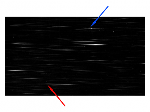 Zdjęcie widm pryzmatycznych obiektów pola gwiazdy V407 Cyg zrobione bez filtrów w nocy 23 IV 2010 r. Czerwoną strzałką oznaczono efekt blendowania się kilku obiektów, niebieską - gwiazdę V407 Cyg. Widma, z którymi pracują astronomowie są wykonywane na czarno-białych, ale za to bardzo czułych kamerach. Nie potrzebują widzieć kolorów tęczy, ponieważ sami precyzyjnie dopasowują długości fal do elementów widma. Widoczne tutaj spektra są „surowe”, czyli nie poddane żadnej redukcji, w związku z tym nie widać w ni