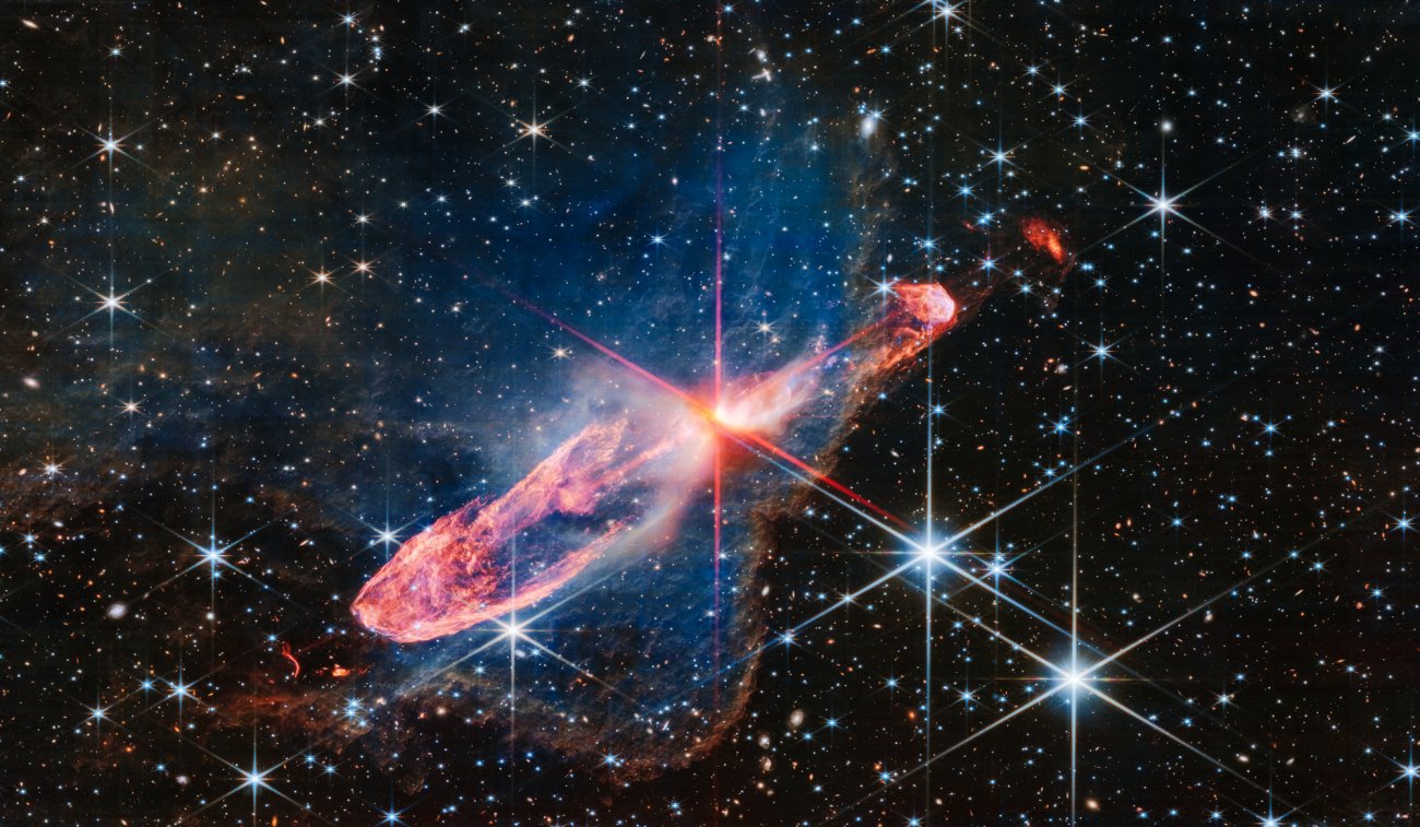 Teleskop Webba sfotografował w wysokiej rozdzielczości za pomocą kamery NIRCam (bliska podczerwień) ściśle ze sobą związaną, aktywną parę tworzących się gwiazd, znaną jako obiekt Herbig-Haro 46/47 (HH 46/47). Rodzące się gwiazdy znajdują się w centrum zdjęcia w pobliżu miejsca, skąd wychodzą charakterystyczne czerwone promienie dyfrakcyjne („spajki”) będące efektem instrumentalnym spowodowanym konstrukcją Teleskopu Webba. Źródło: NASA, ESA, CSA, Joseph DePasquale (STScI)