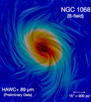Fotografia NGC 1068 po raz pierwszy ukazująca „magnetyczne” ramiona spiralne jej galaktyki macierzystej. Siły wywierane przez pola magnetyczne są zdominowane przez ruch wirowy galaktycznego dysku. W jego efekcie drobiny pyłu obecne ramionach galaktyki ustawiają się zgodnie z ich kierunkiem. Źródło: SOFIA/HAWC+/E. Lopez-Rodriguez
