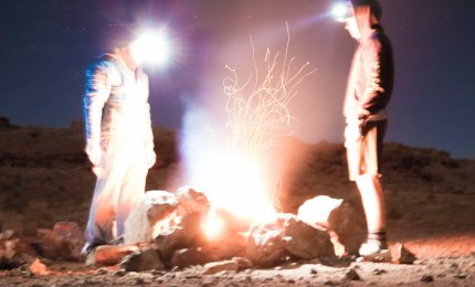 Dwóch mężczyzn stojących nocą przy ognisku