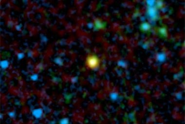   Zdjęcie z Kosmicznego Teleskopu Spitzera ukazane w sztucznych kolorach przedstawia odległą galaktykę (kolor żółty) goszczącą kwazar - supermasywną czarną dziurę otoczoną przez pierścień lub też torus gazu i pyłu. "Podczerwone oczy" teleskopu przeniknęły przez pył by odnaleźć ten ukryty obiekt zdający się być członkiem długo poszukiwanej grupy brakujących kwazarów. Zielone i niebieskie plamki to galaktyki nie zawierające kwazarów. Źródło: NASA/JPL-Caltech/A. Martinez-Sansigre (Oxford University).