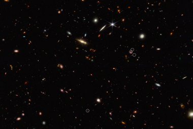 Na ilustracji: Układ 10 galaktyk oznaczonych ośmioma, białymi kółkami wzdłuż przekątnej, nitkowatej linii (dwa kółka zawierają więcej niż jedną galaktykę), który został sfotografowany przez Teleskop Webba z kamerą NIRCam. Jest to rozciągające się na 3 miliony l.św. włókno zakotwiczone do jasnego kwazara J0305-3150 (widać go w centrum grupy trzech kółek po prawej stronie zdjęcia). Te 10 galaktyk istniało już 830 milionów lat po Wielkim Wybuchu (z=6,6).Źródło:NASA, ESA, CSA, Feige Wang,Joseph DePasquale(STScI
