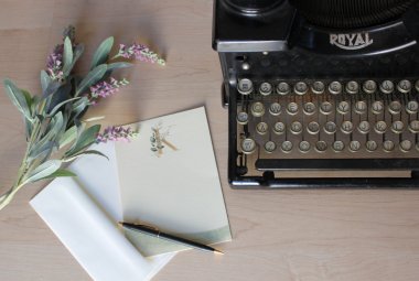Maszyna do pisania, obok papeteria i kwiaty szałwii.