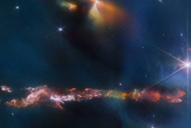 Na ilustracji: Obraz okolic obiektu Herbig-Haro 797 (HH 797) sfotografowany w bliskiej podczerwieni (8 barw o długościach fali od 1,64 μm do 4,7 μm) przez kamerę NIRCam znajdującą się na pokładzie Kosmicznego Teleskopu Jamesa Webba. W dolnej części jego części widać wąską mgławicę o jaskrawych barwach rozciągającą się poziomo przez cały kadr – z większą różnorodnością po jej prawej stronie.  Źródło: ESA/Webb, NASA & CSA, T. Ray (Dublin Institute for Advanced Studies)